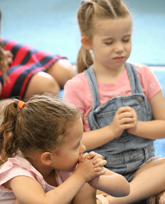 Two young girls sitting and meditating, one holding foot, both with eyes closed. Pre-K & Kindergarten | Immanuel Lutheran School | Belvidere, IL