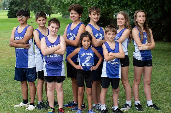 Cross-country team poses on grass, wearing blue and white singlets, arms crossed. Athletics | Immanuel Lutheran School | Belvidere, IL