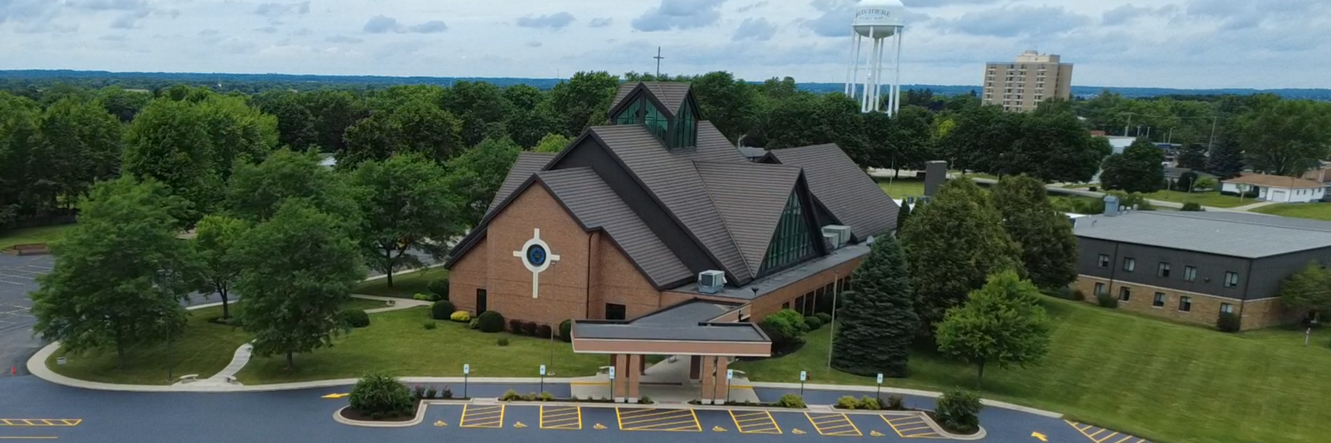 Church building with a brown roof and a water tower in the distance. Elementary School | Immanuel Lutheran School | Belvidere, IL
