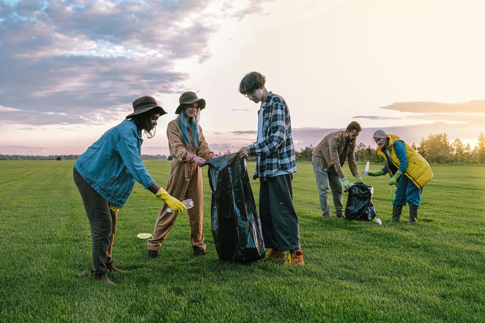 People picking up trash in a grassy field, placing litter into black bags. Discipleship | Immanuel Lutheran School | Belvidere, IL