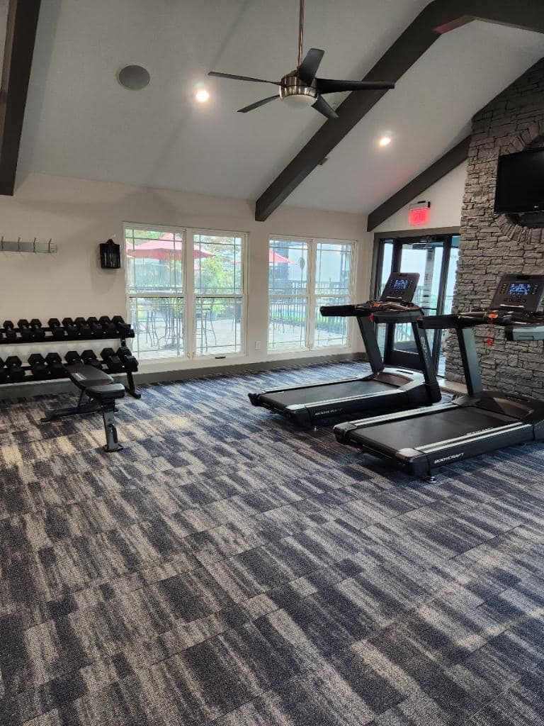 A gym with treadmills , dumbbells , and a ceiling fan.