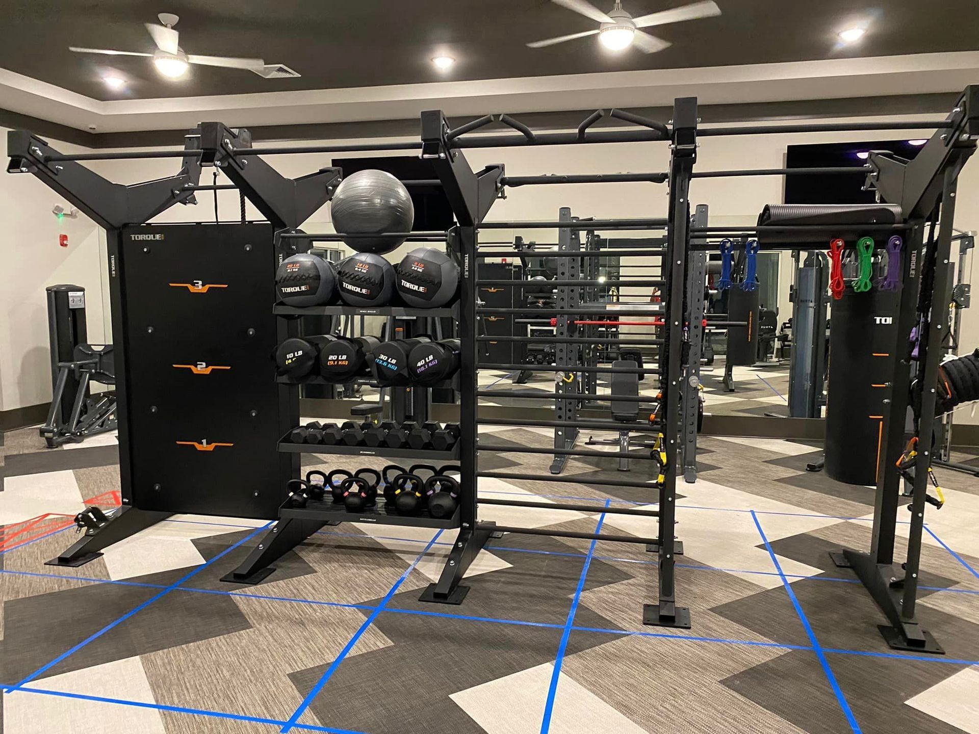 A gym with a lot of equipment and a ceiling fan.