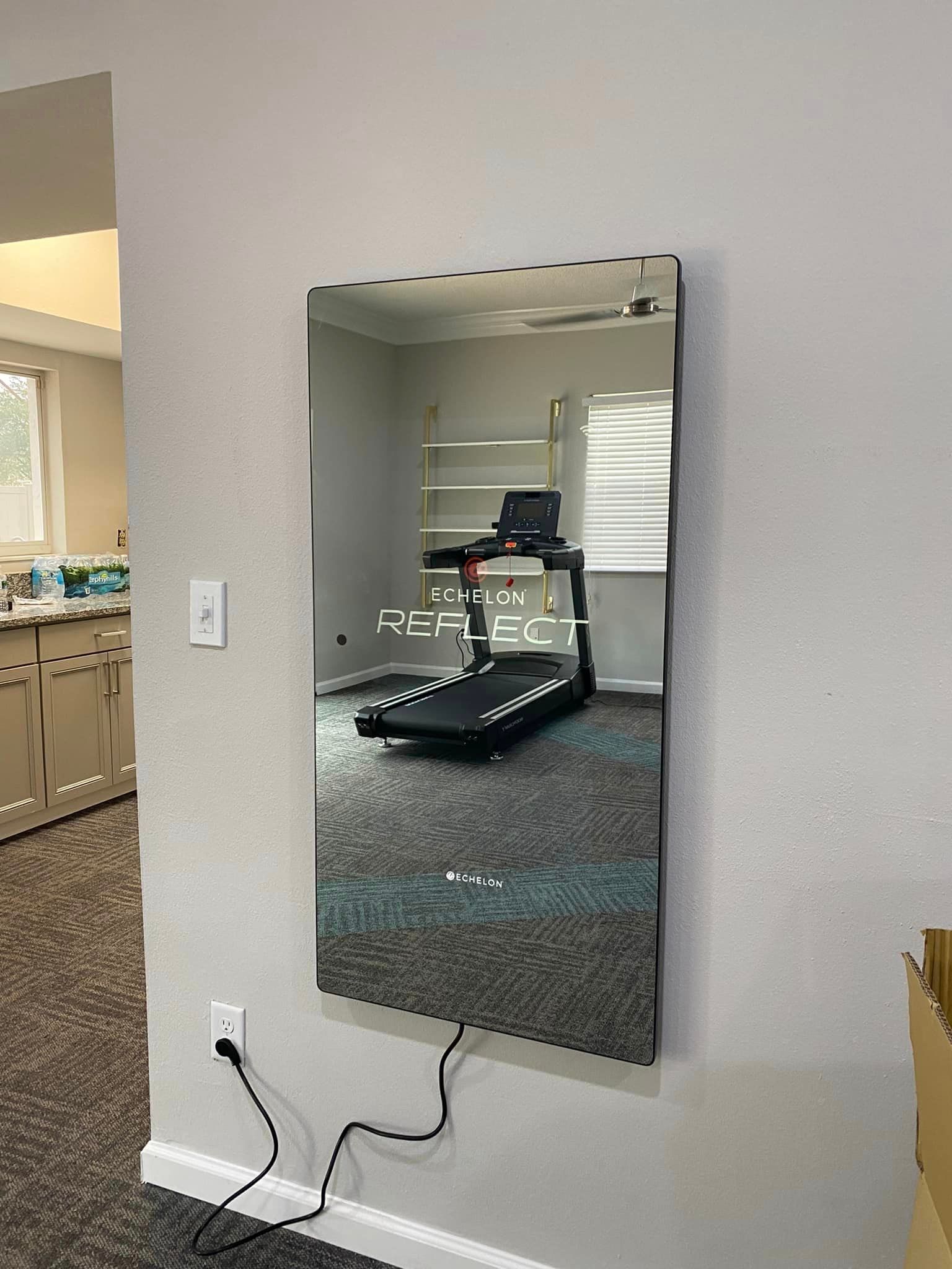 A treadmill is reflected in a mirror on a wall.