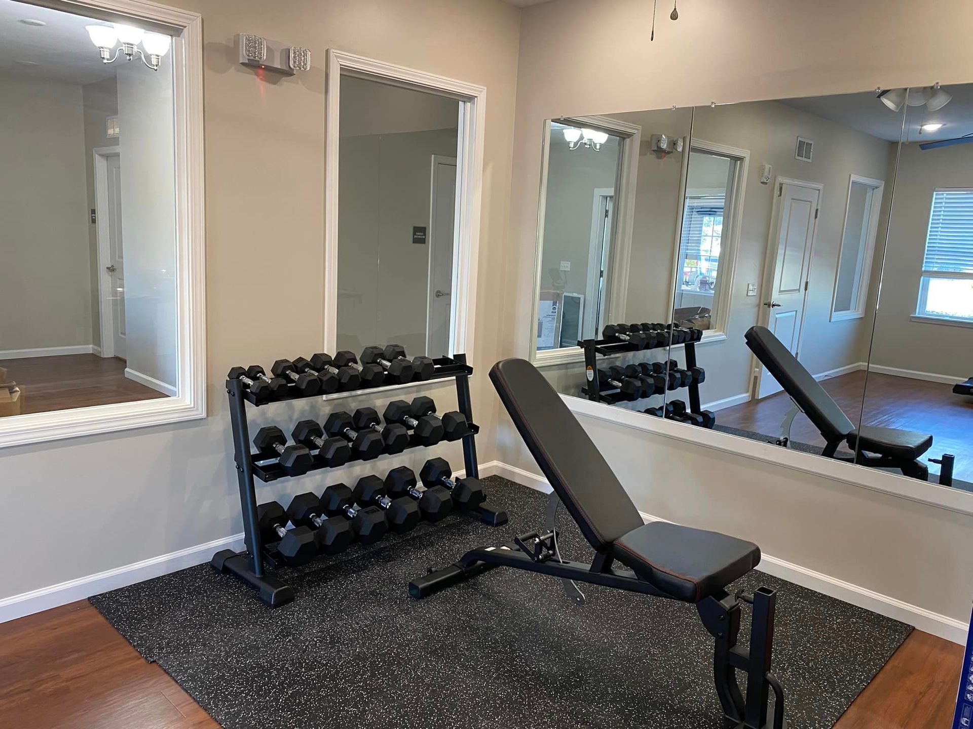 A gym with a bench , dumbbells , and a large mirror.