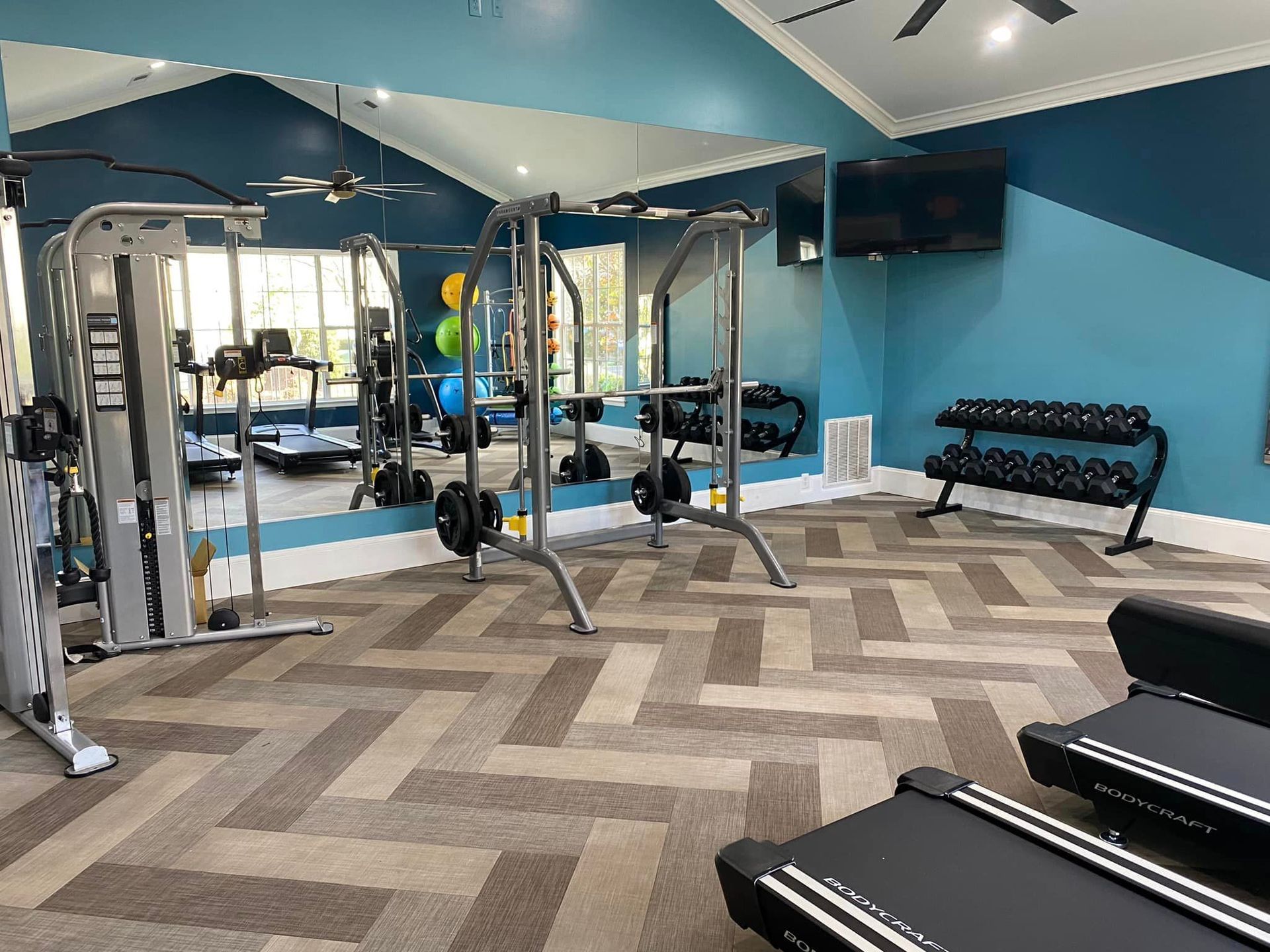 A gym with a treadmill , dumbbells , and a large mirror.