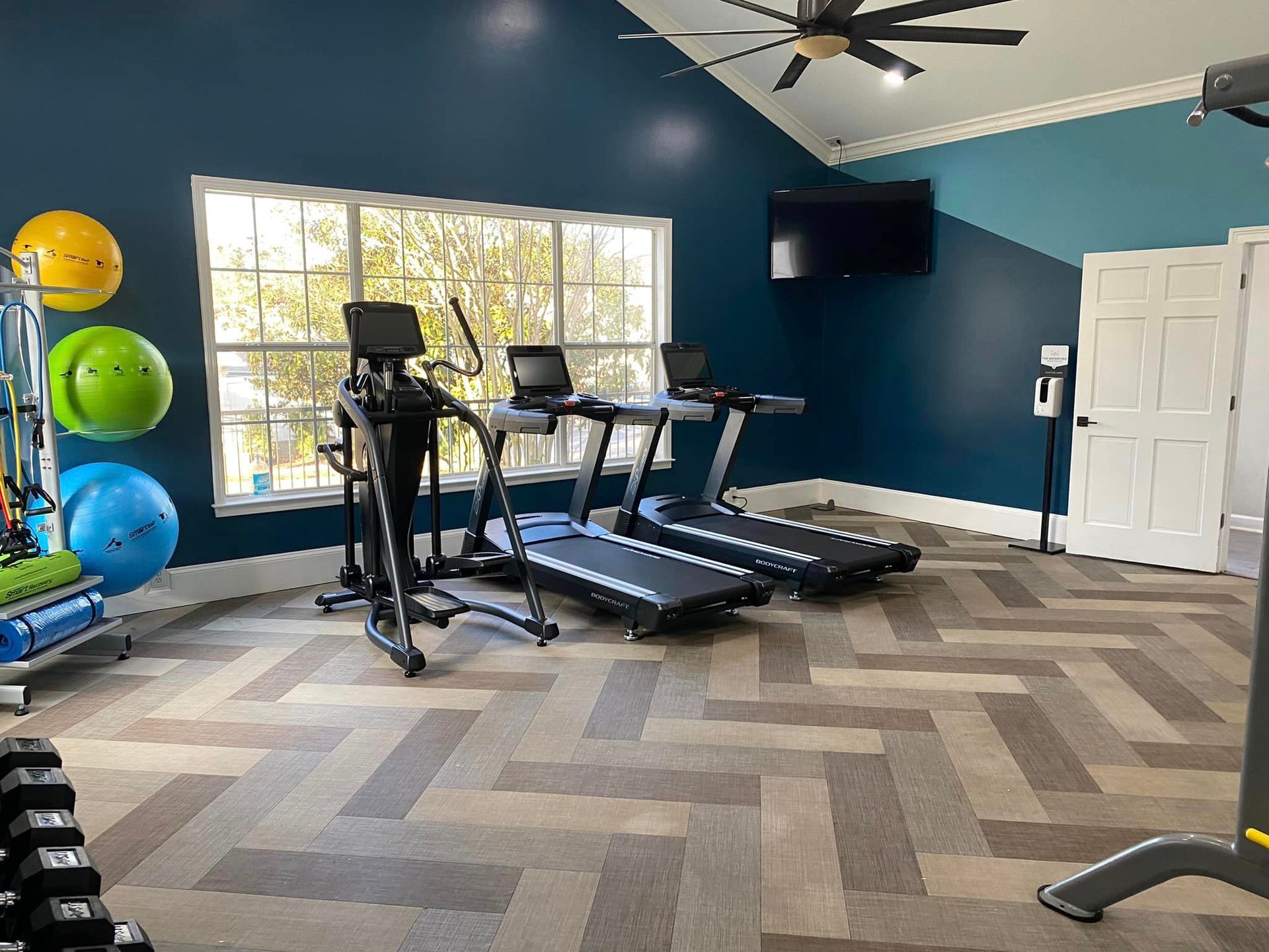 A gym with treadmills , exercise bikes , dumbbells and a television.