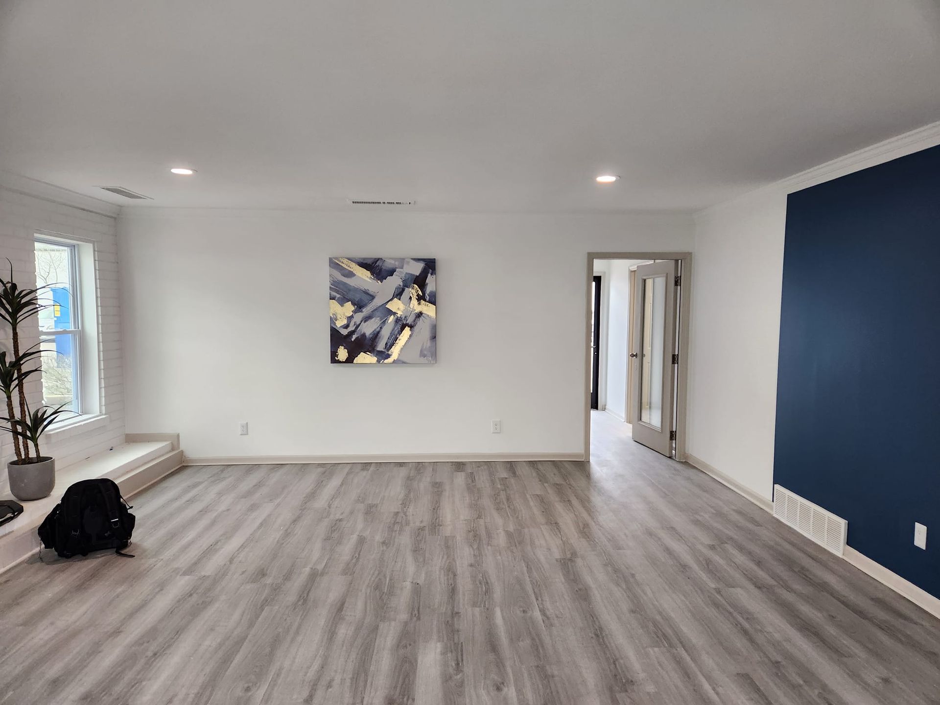 An empty living room with a blue wall and a painting on the wall.