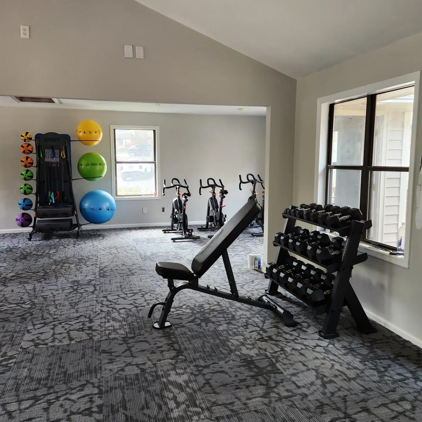 A gym with a bench , dumbbells , and exercise bikes.