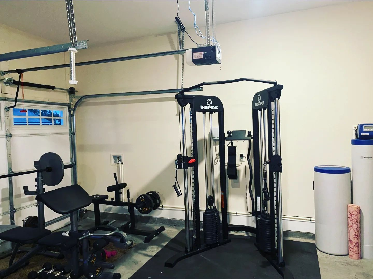 A garage with a lot of exercise equipment and a garage door open