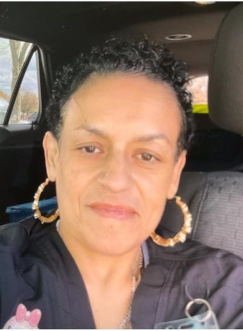Woman with short curly hair, gold hoop earrings, and black top smiles inside a car.
