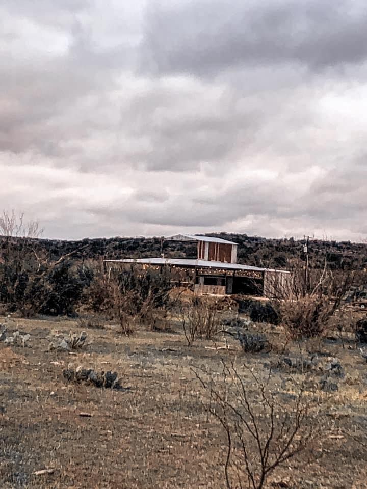 A house in the middle of a field with a cloudy sky in the background.