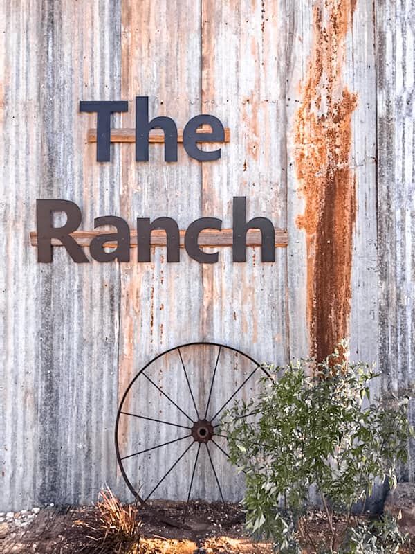 A sign that says the ranch with a wagon wheel in front of it