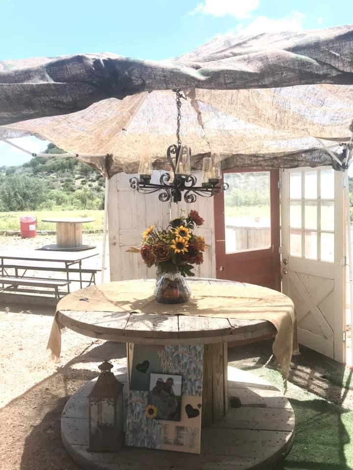 A wooden table with a vase of flowers on it under an umbrella.