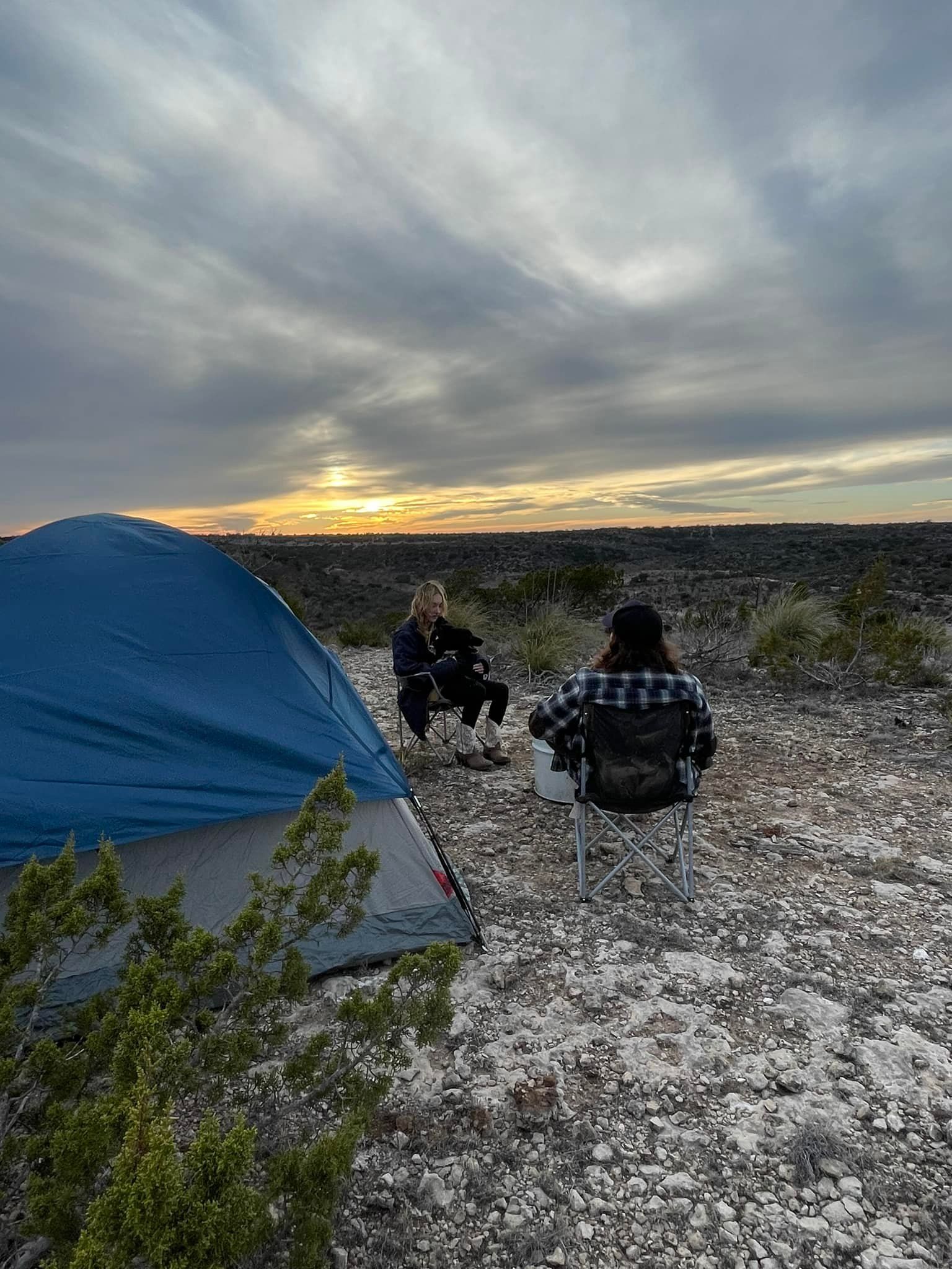 Two people are sitting in chairs in front of a tent.