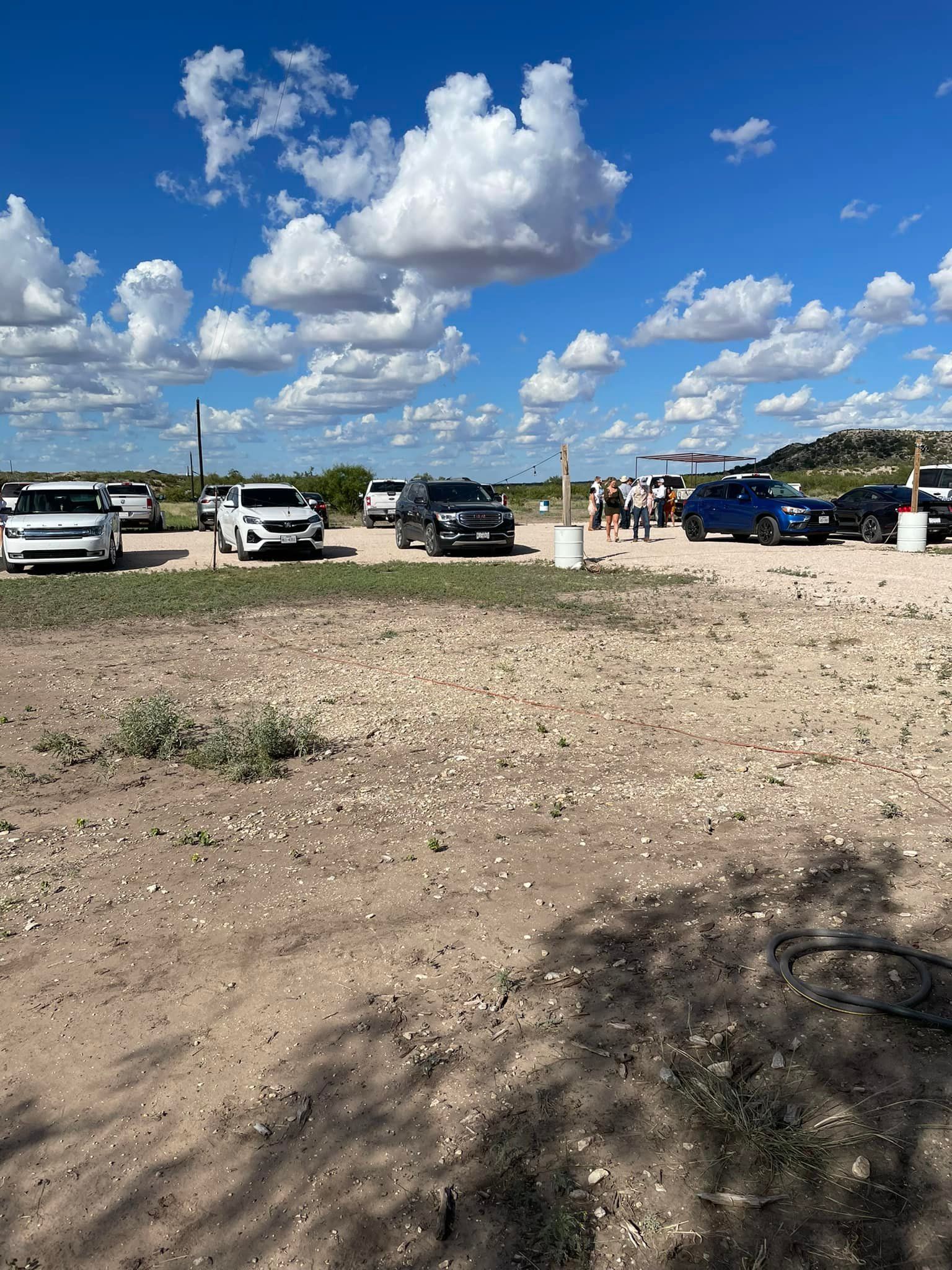 A group of cars are parked in a dirt field.