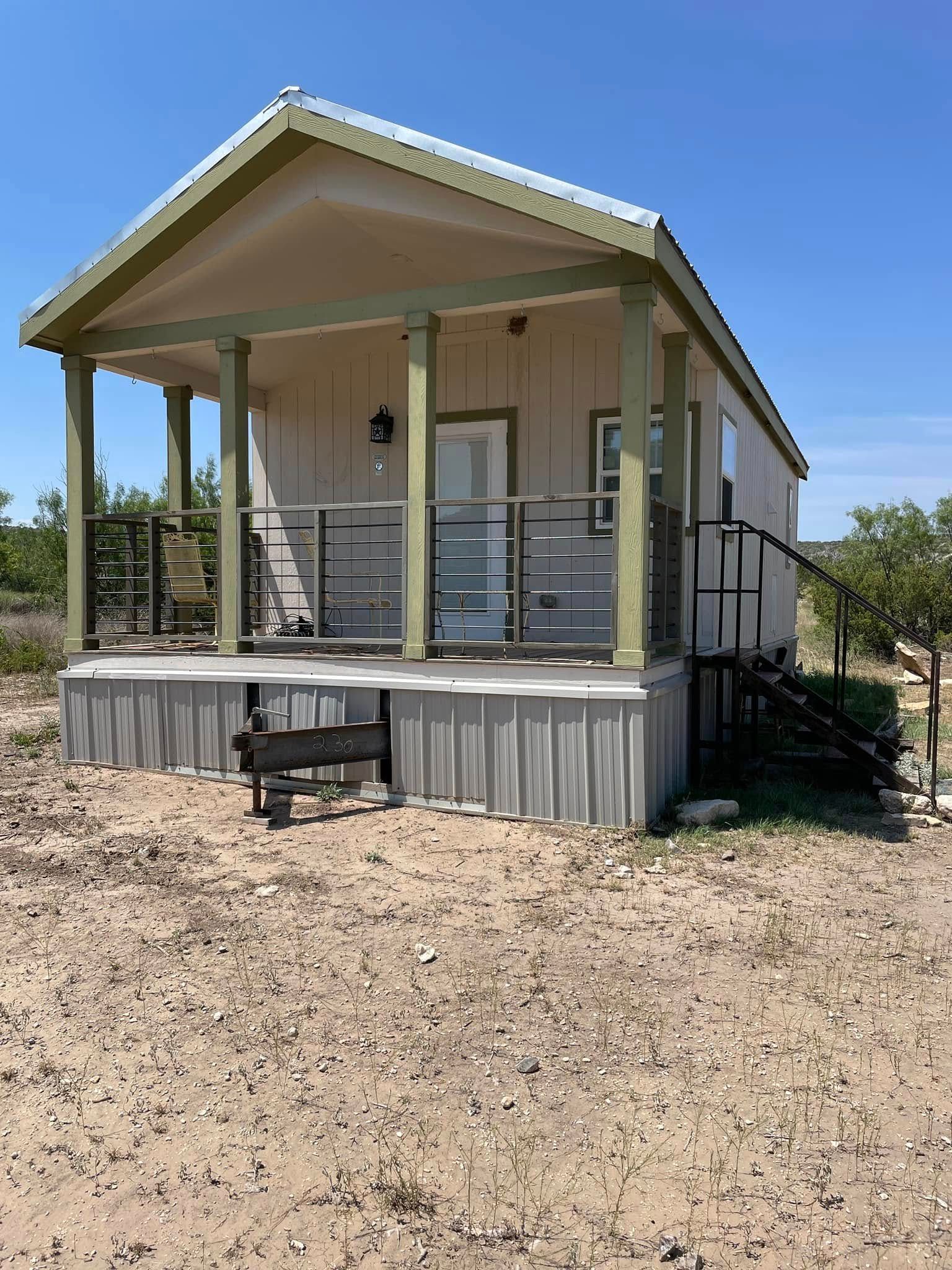 A small house with a porch in the middle of a dirt field.