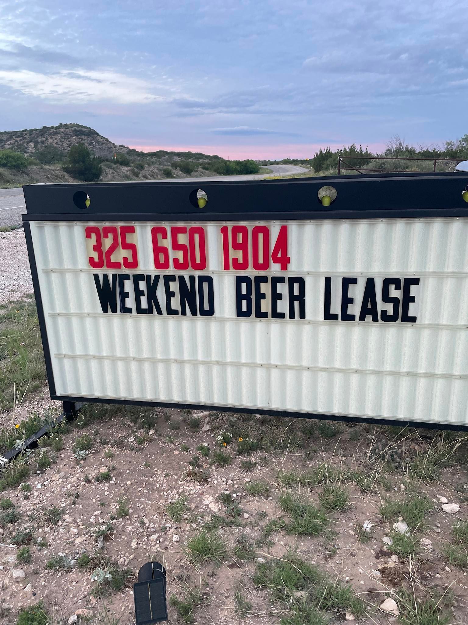 A sign that says `` 325 650 1904 weekend beer lease '' is sitting in a field.
