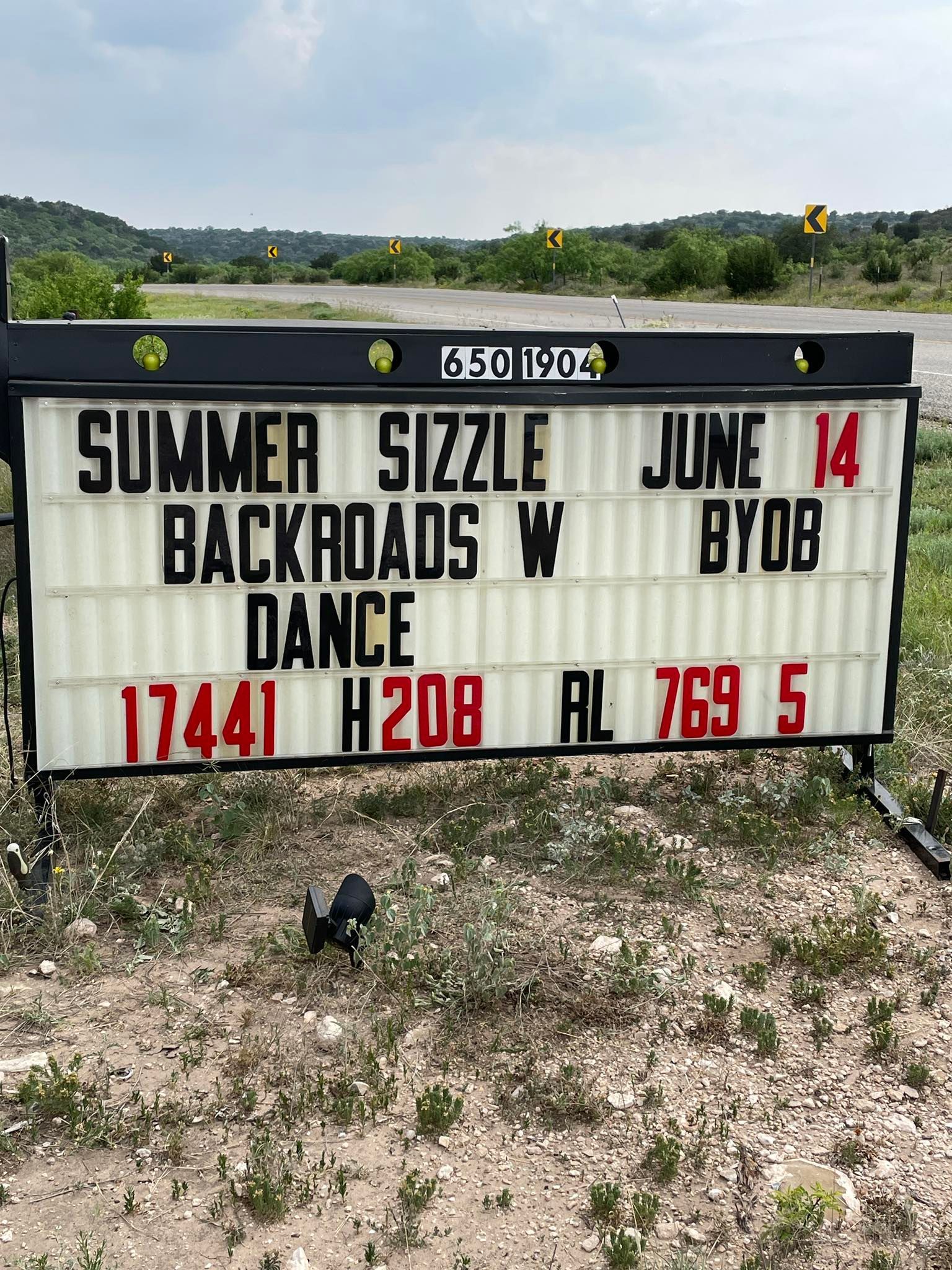 A sign that says summer sizzle backroads w dance is in a field.