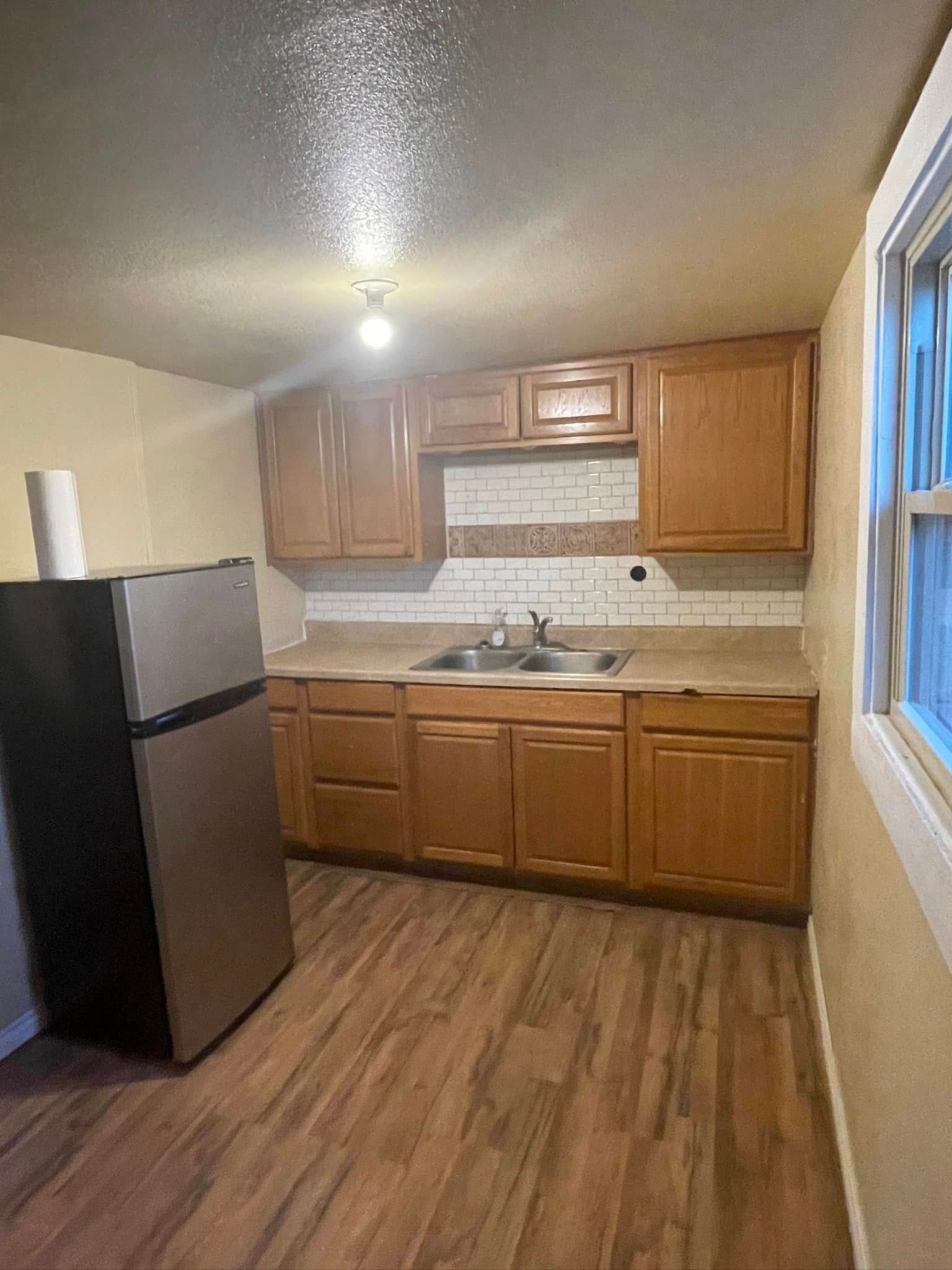 A kitchen with wooden cabinets , a stainless steel refrigerator , a sink , and a window.