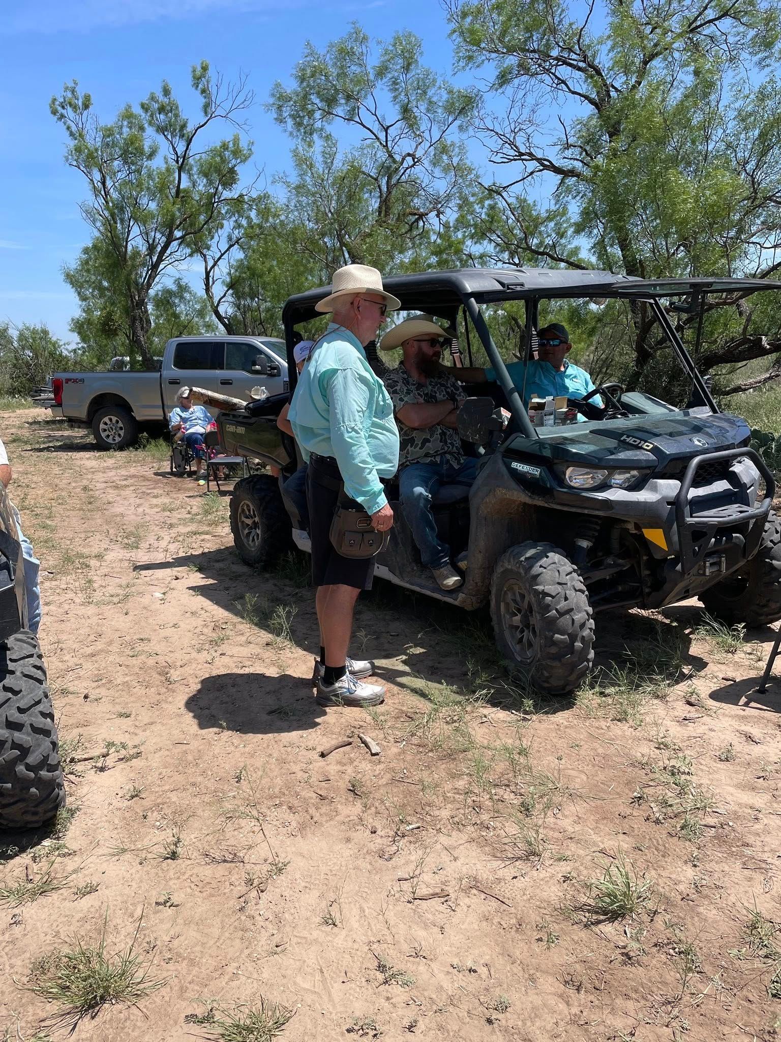 A group of men are standing next to a atv in a dirt field.