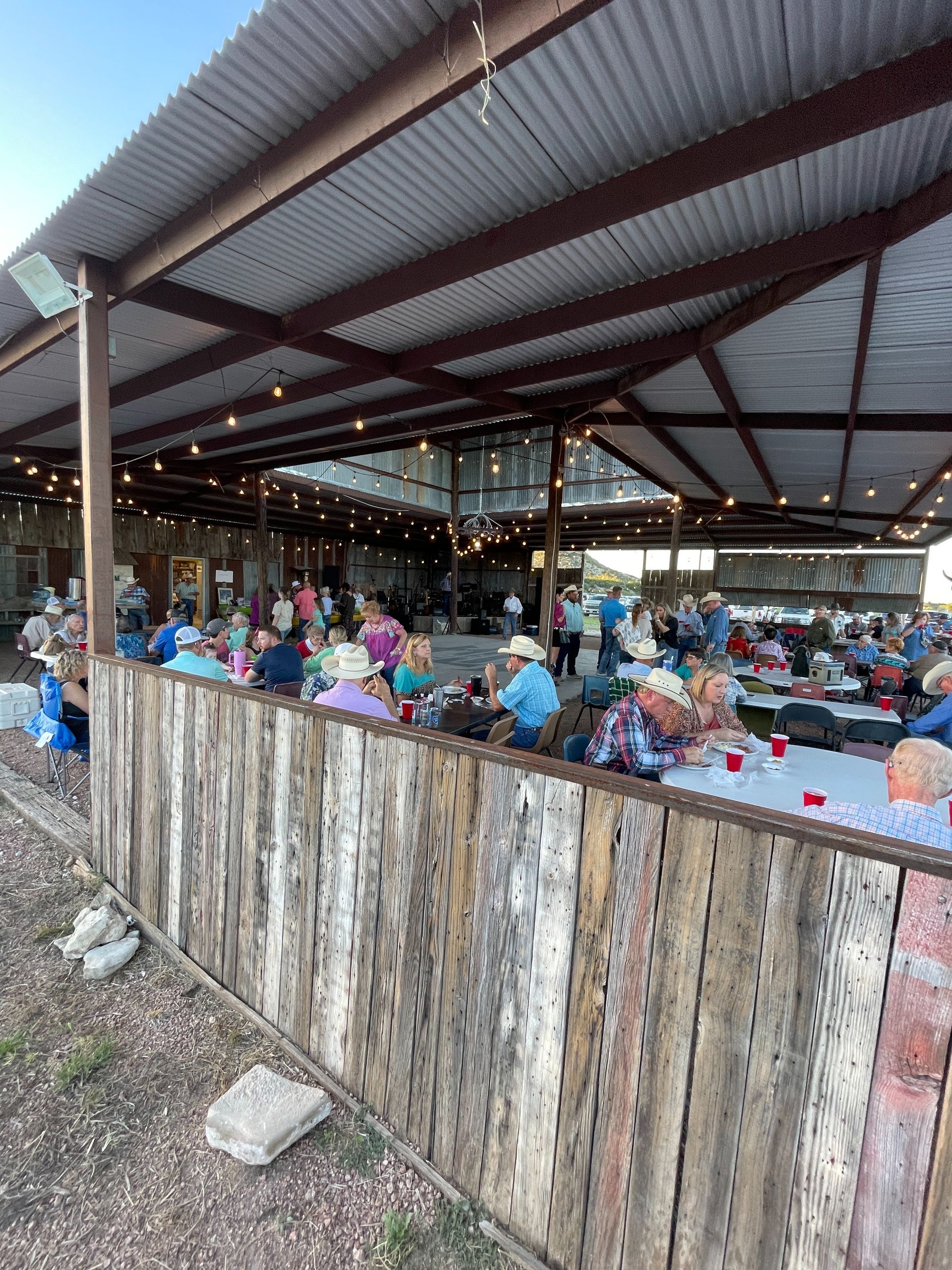 A group of people are sitting at tables under a covered area.