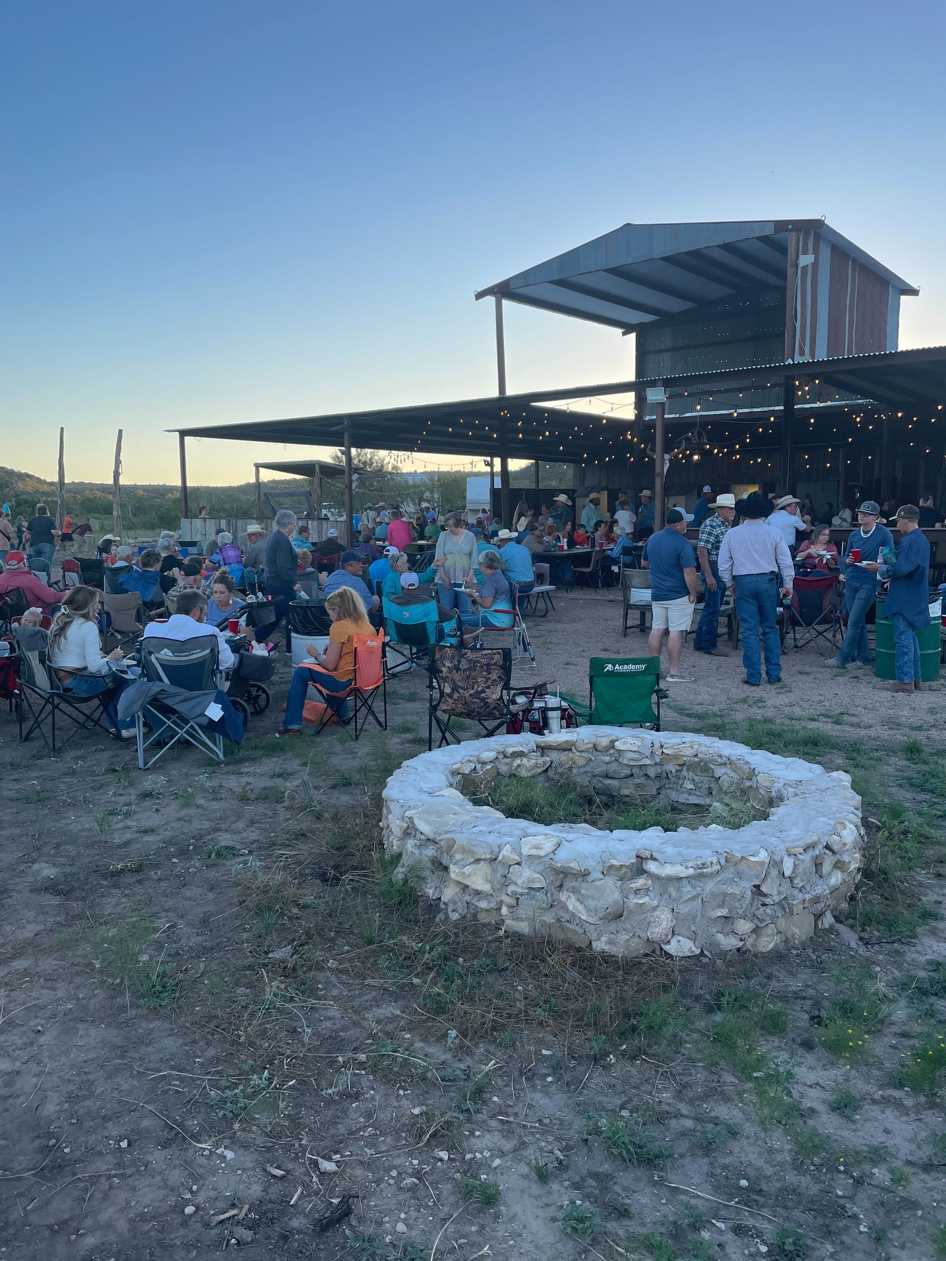 A group of people are sitting around a fire pit in a field.