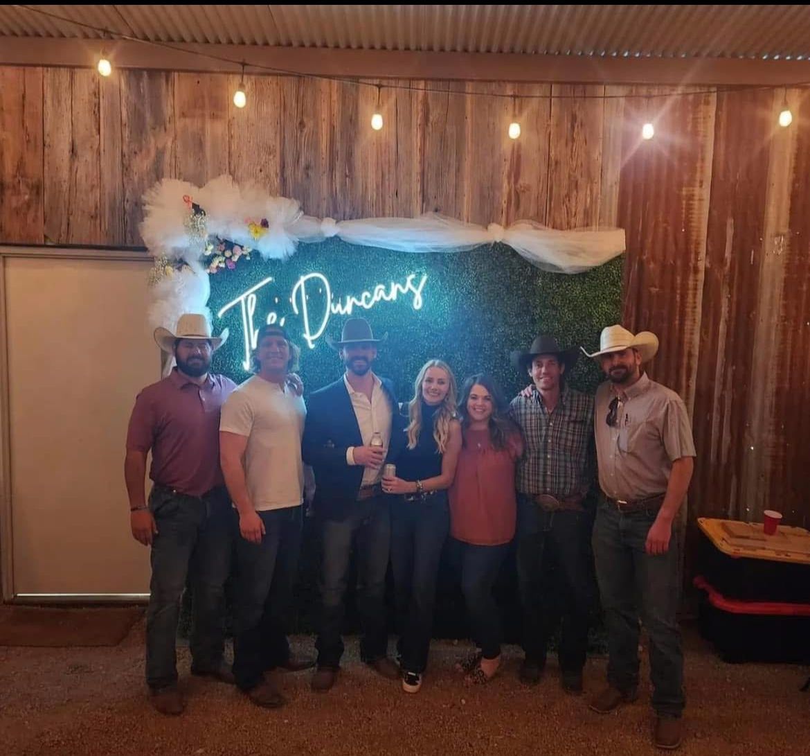 A group of people standing in front of a neon sign that says t. duncan 's