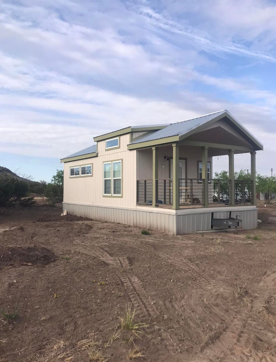 A small house with a porch is sitting in the middle of a dirt field.