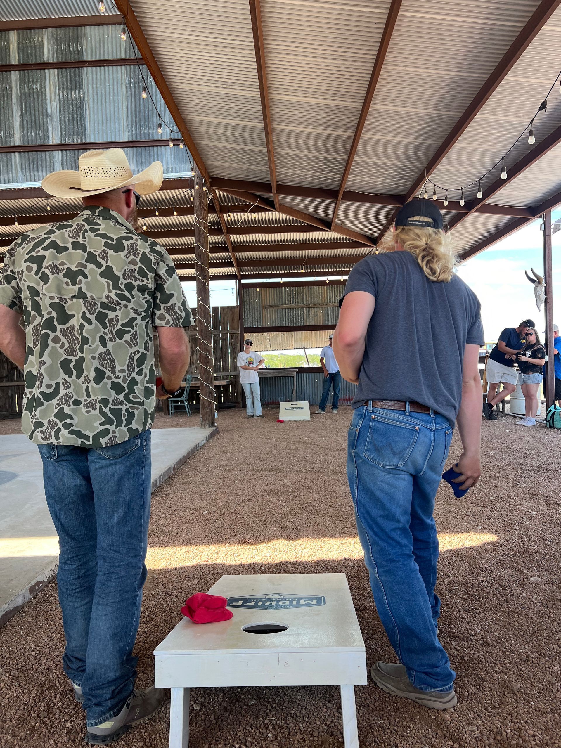 Two men are standing next to each other in front of a cornhole board.