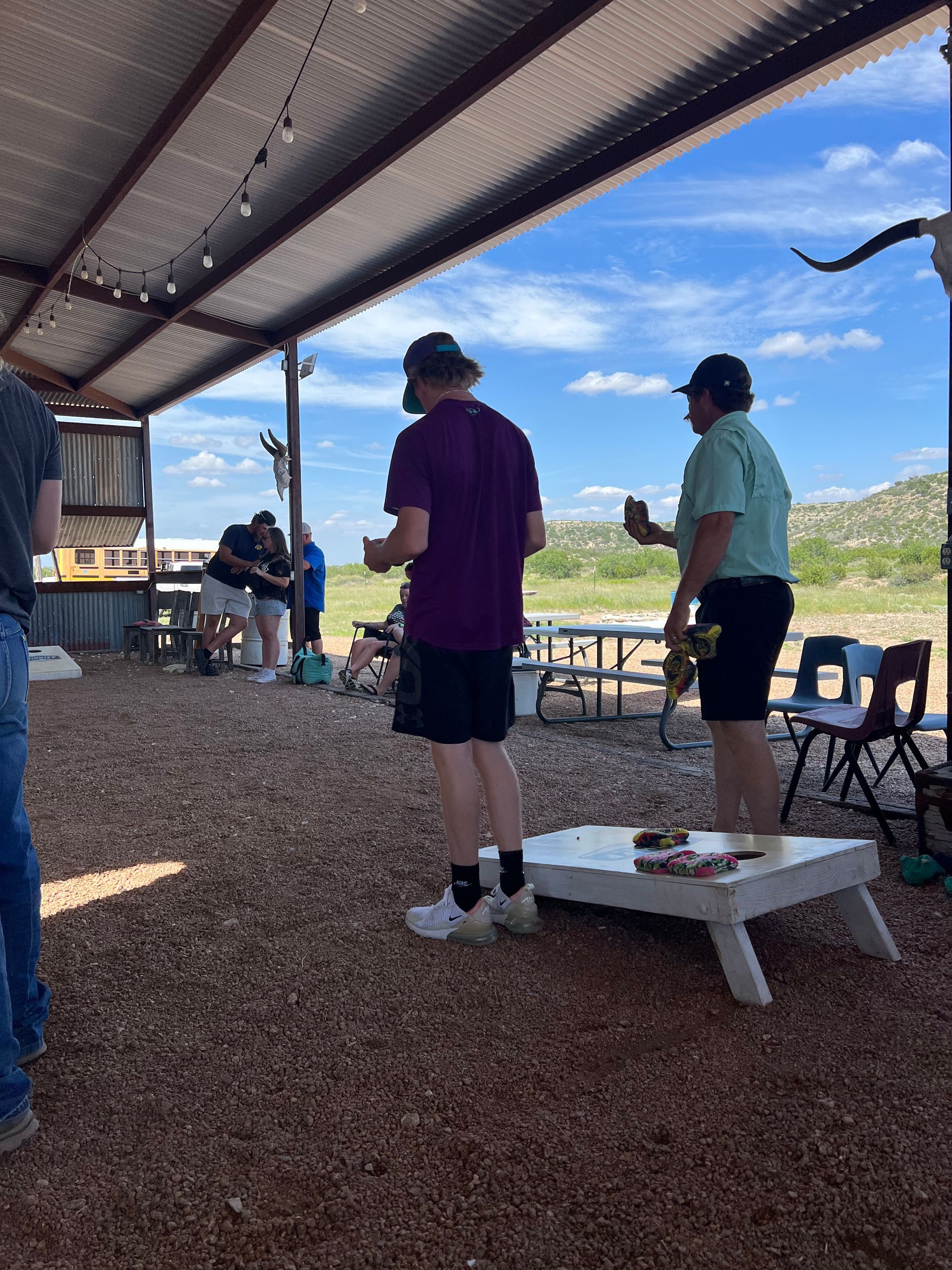A group of people are playing a game of cornhole under a canopy.