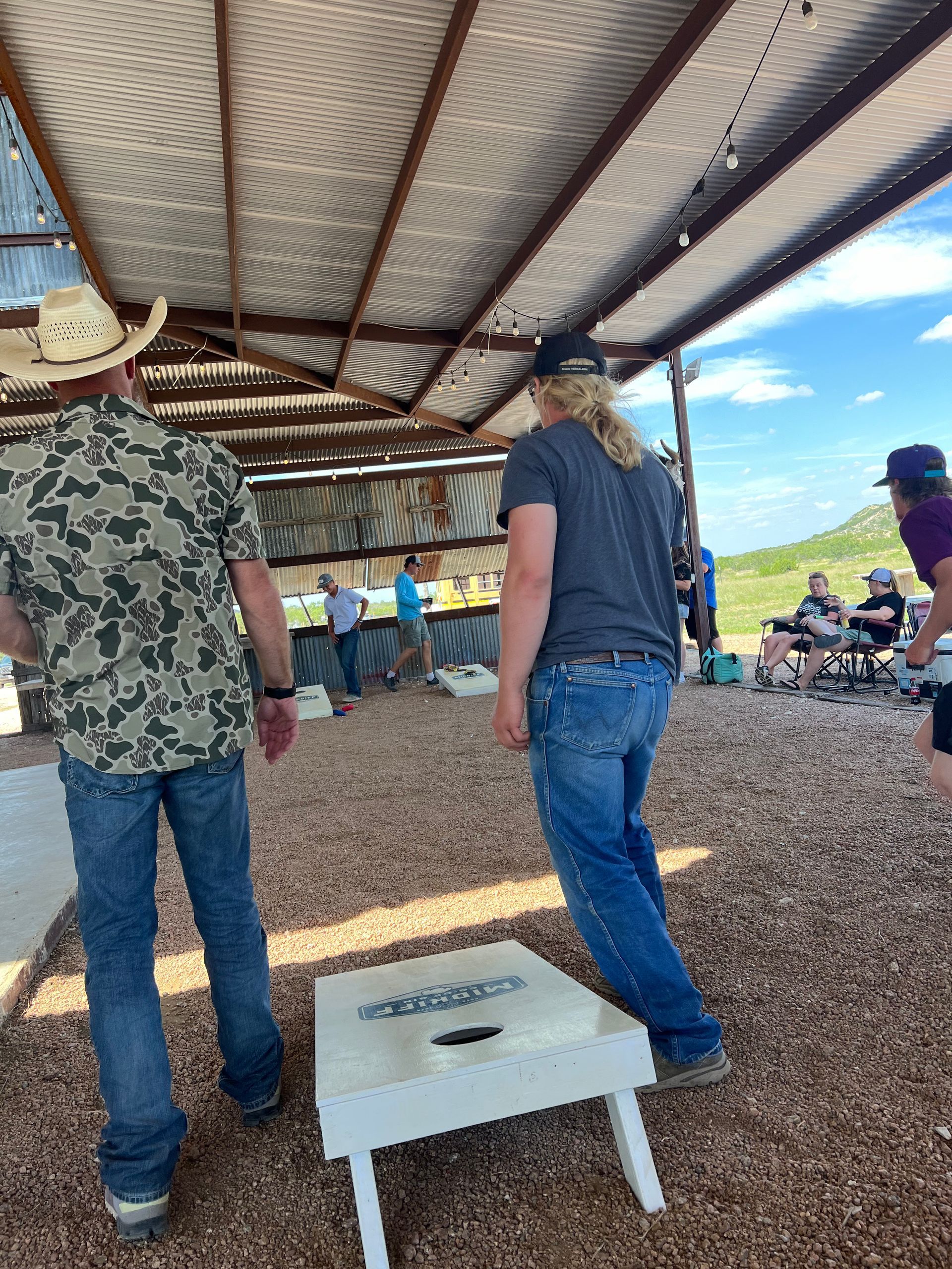 A group of people are playing a game of cornhole in a covered area.