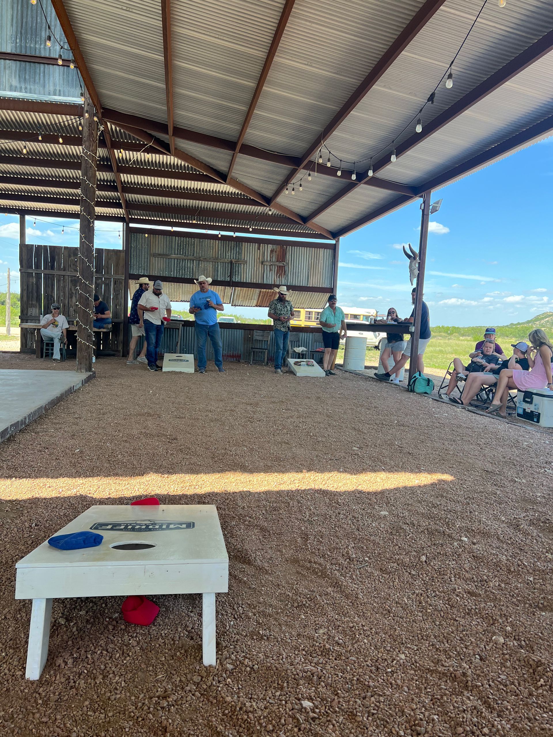 A group of people are playing a game of cornhole under a covered area.
