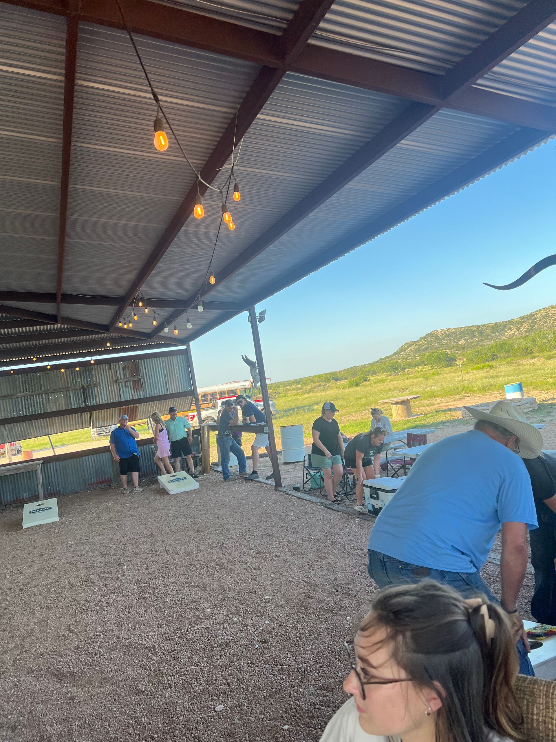 A group of people are playing a game of cornhole under a covered area.