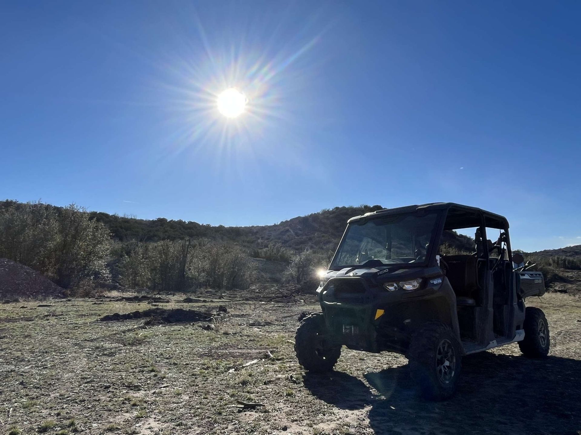 A black atv is parked in a dirt field with the sun shining brightly in the background.