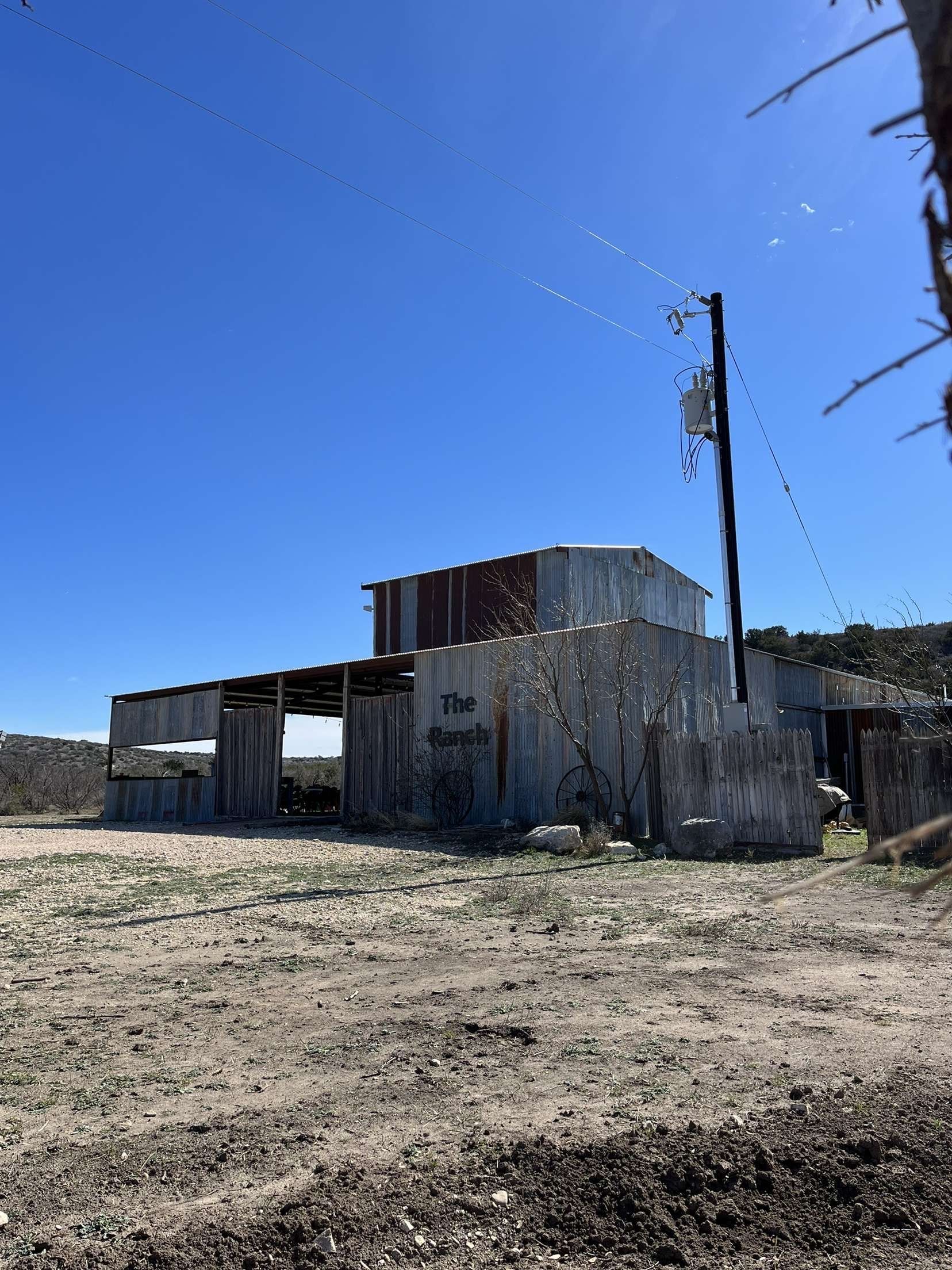 An old building in the middle of a dirt field with a blue sky in the background.