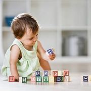 A baby sitting on the floor is playing with colorful alphabet blocks indoors.