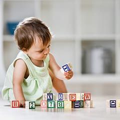 A baby sitting on the floor is playing with colorful alphabet blocks indoors.