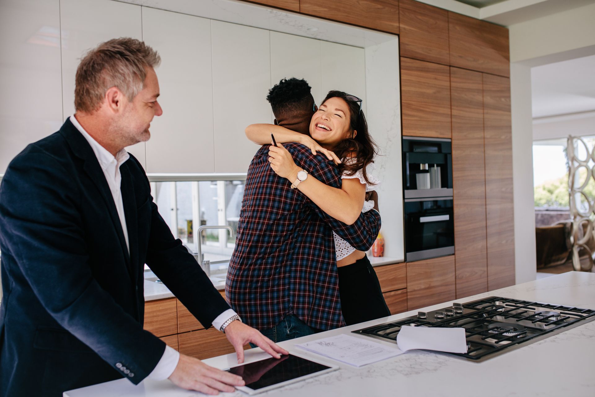 Happy new property owners are embracing each other next to a residential real estate consultant.