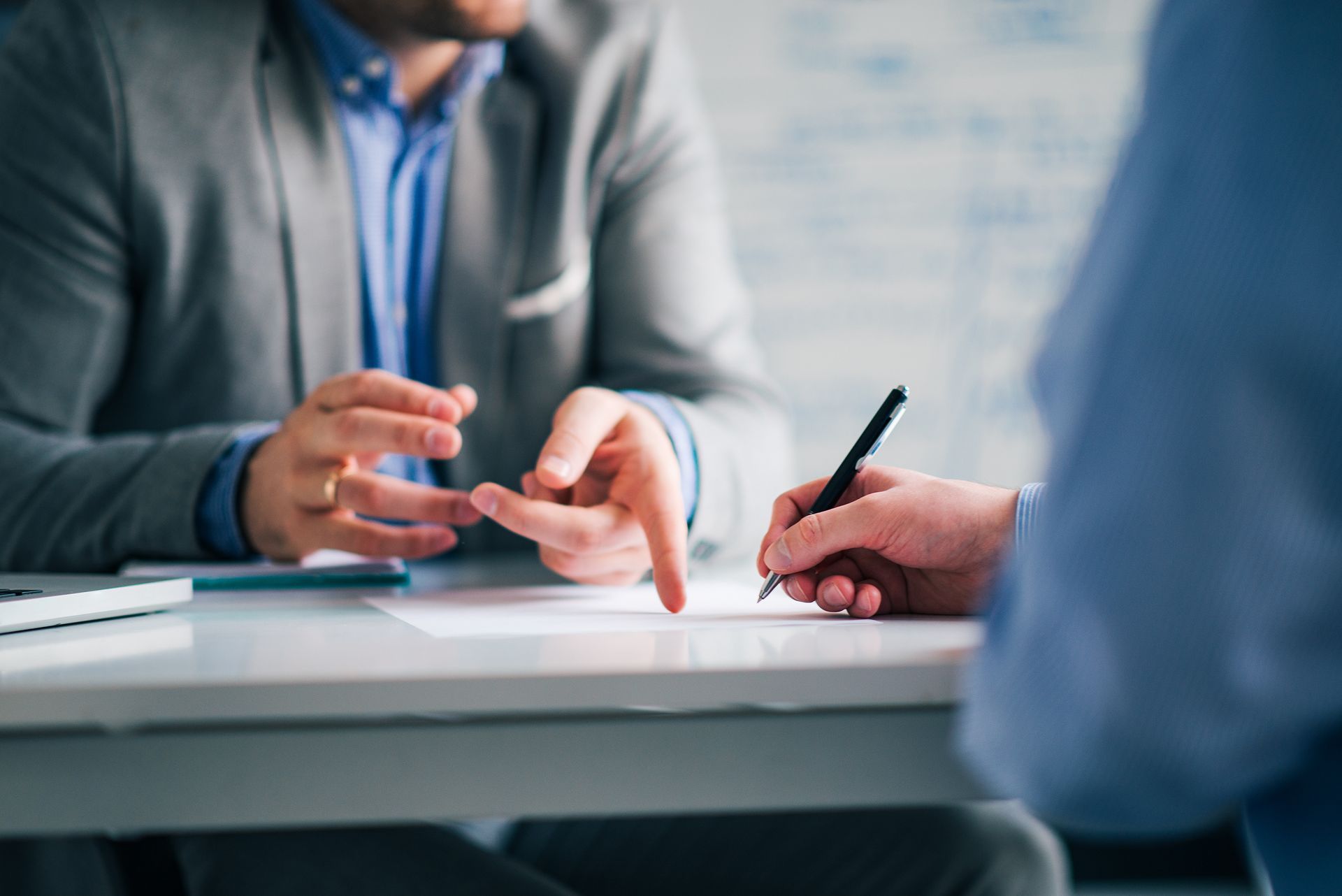 Person in suit points at document as another signs at a desk.