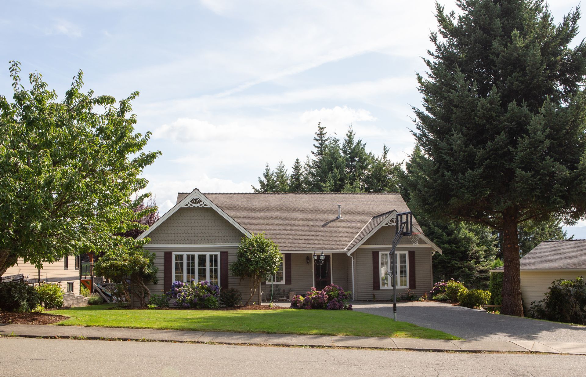 Brown house with green lawn, trees, and cloudy sky.