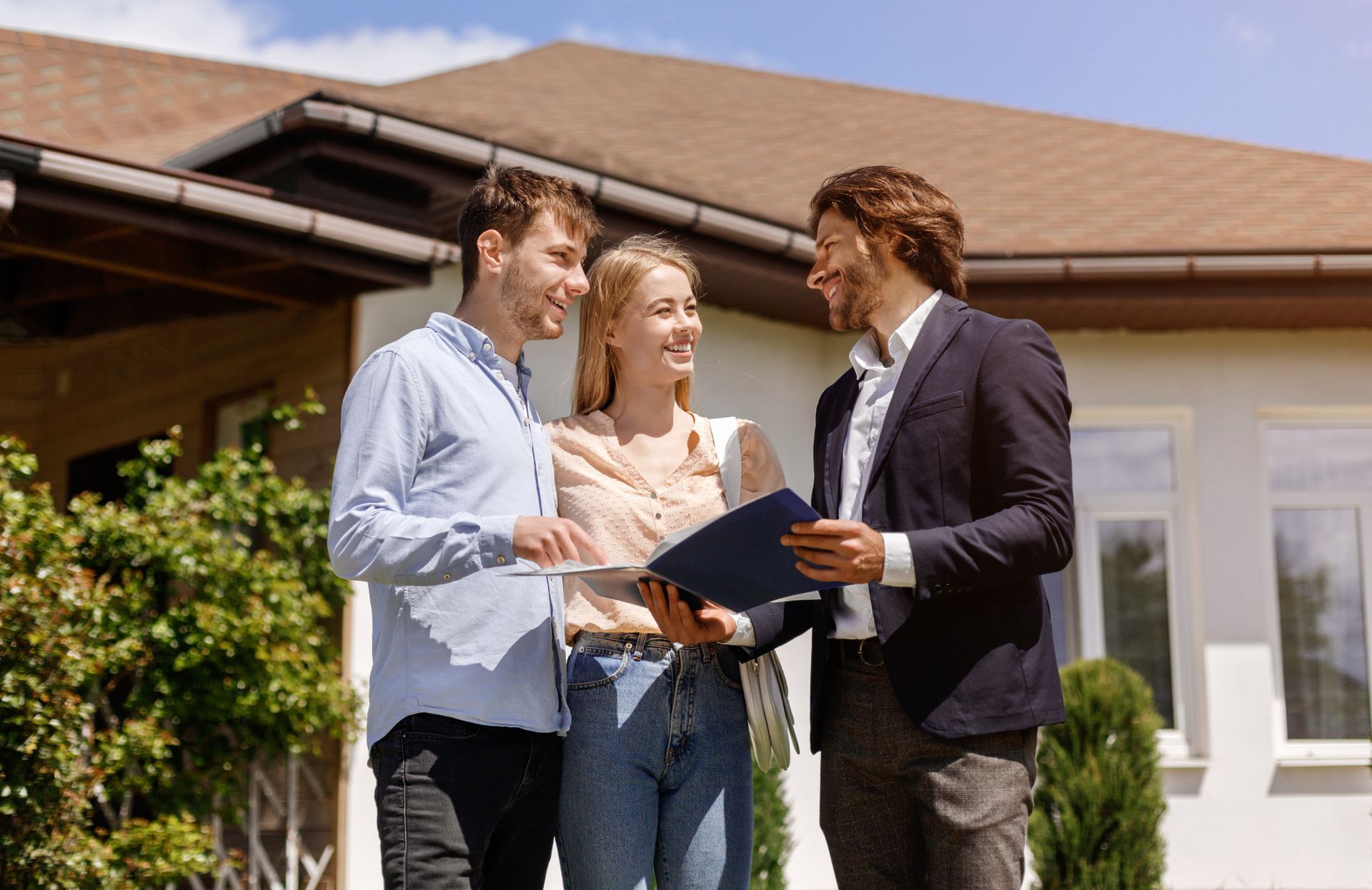 Real estate agent showing paperwork to a smiling couple in front of a house.