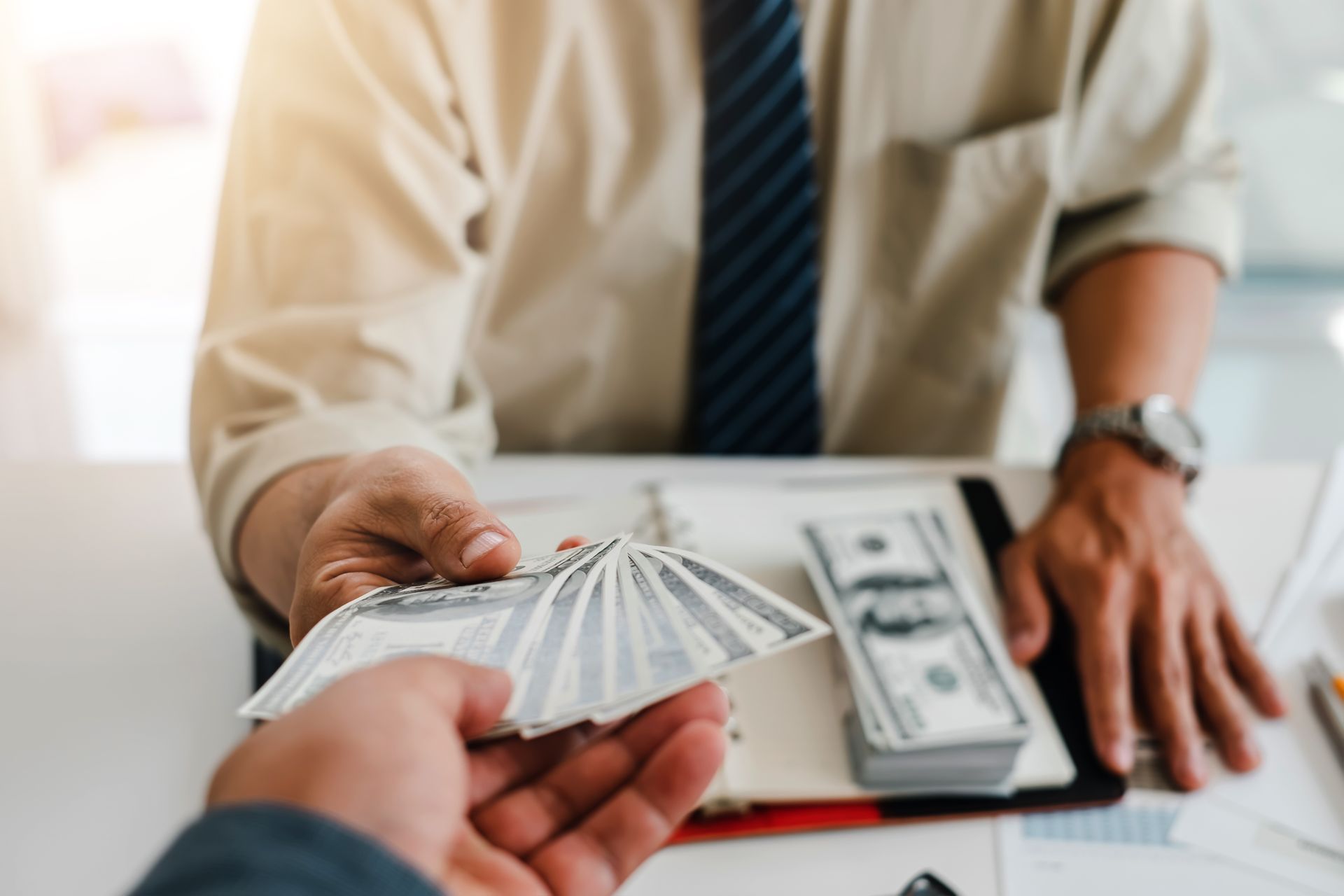 Man handing stack of US dollar bills to another person.