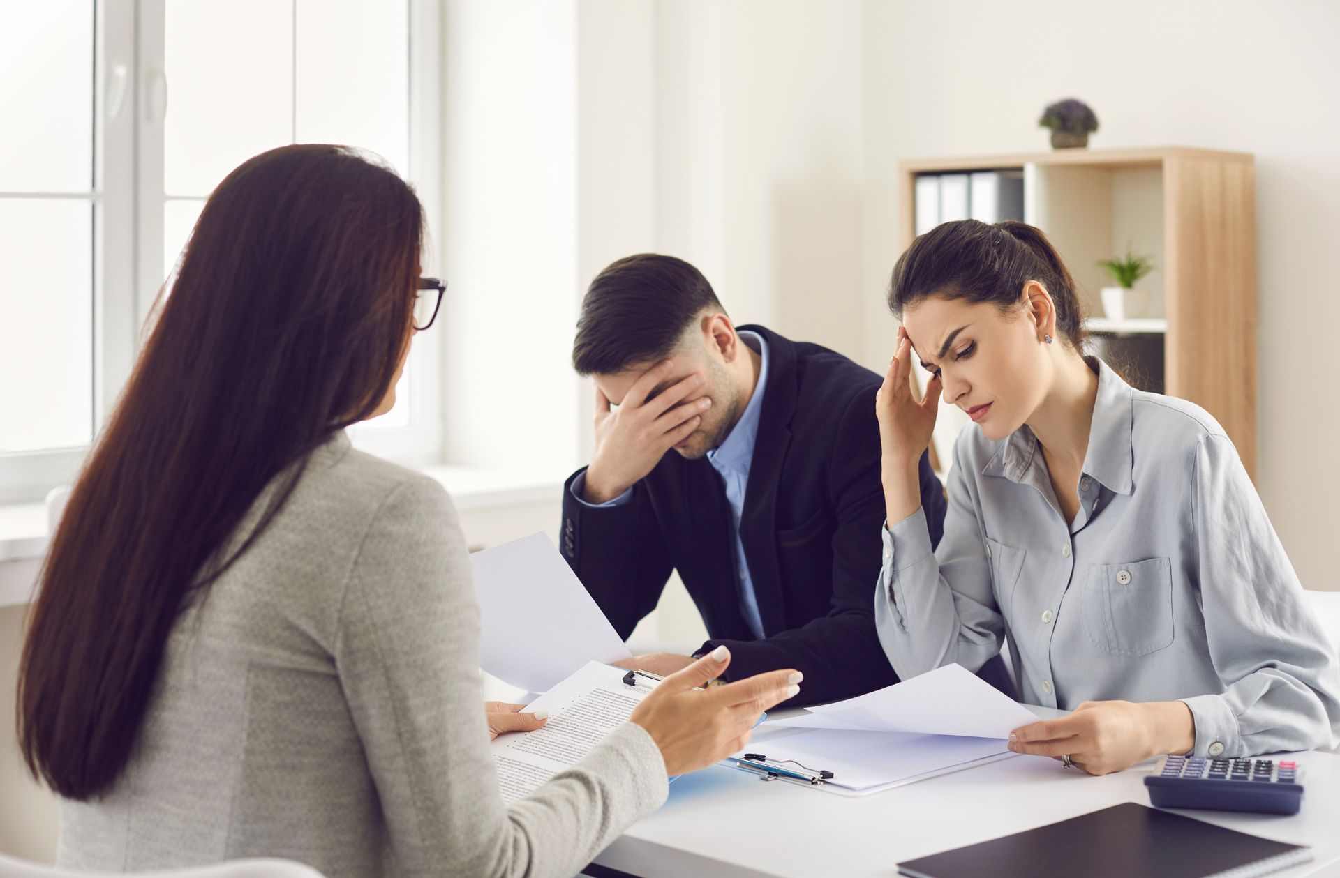 Woman advising distressed couple at a table, looking at documents.