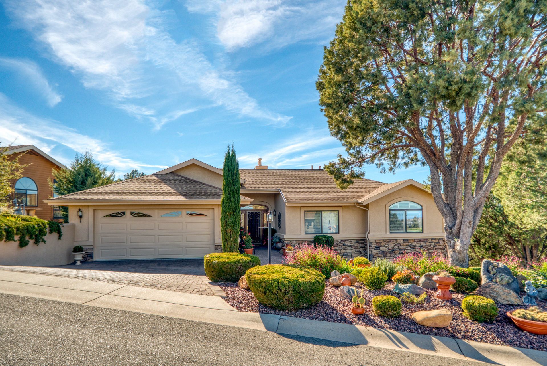 Tan stucco house with rock accents, landscaped yard, blue sky.