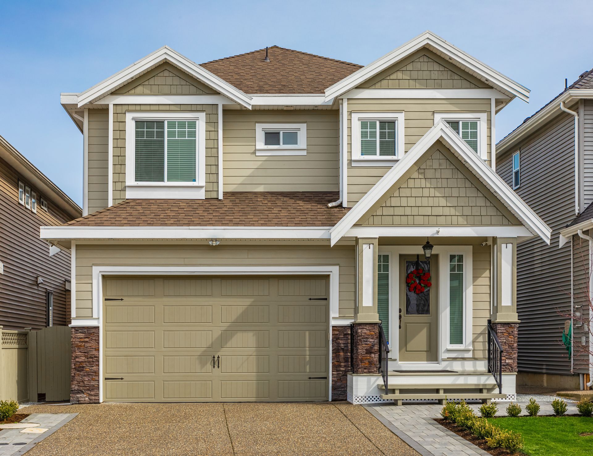 Two-story house with green siding, brown roof, and attached garage. A red wreath hangs on the front door.