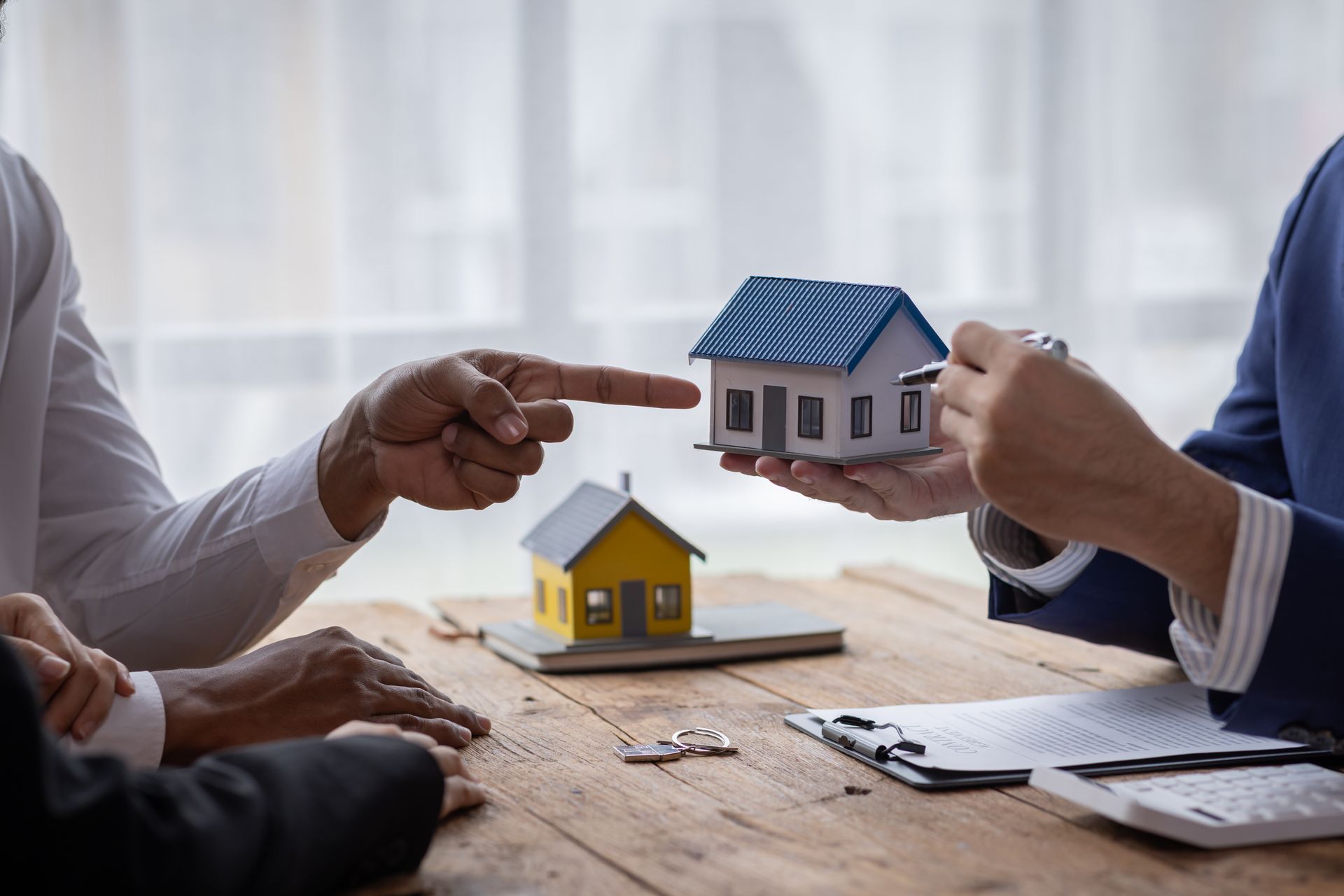 People interacting with miniature houses on a table, possibly real estate transaction.