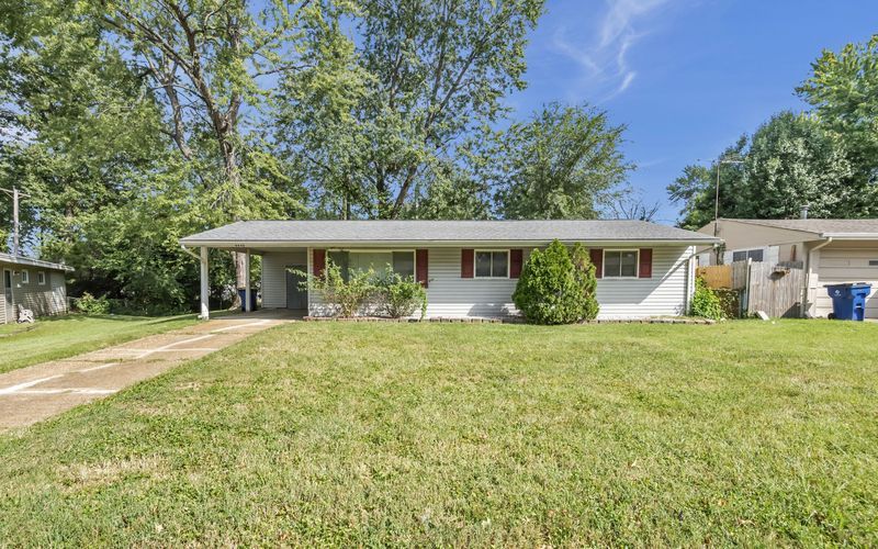 A small white house with a green trash can in front of it.