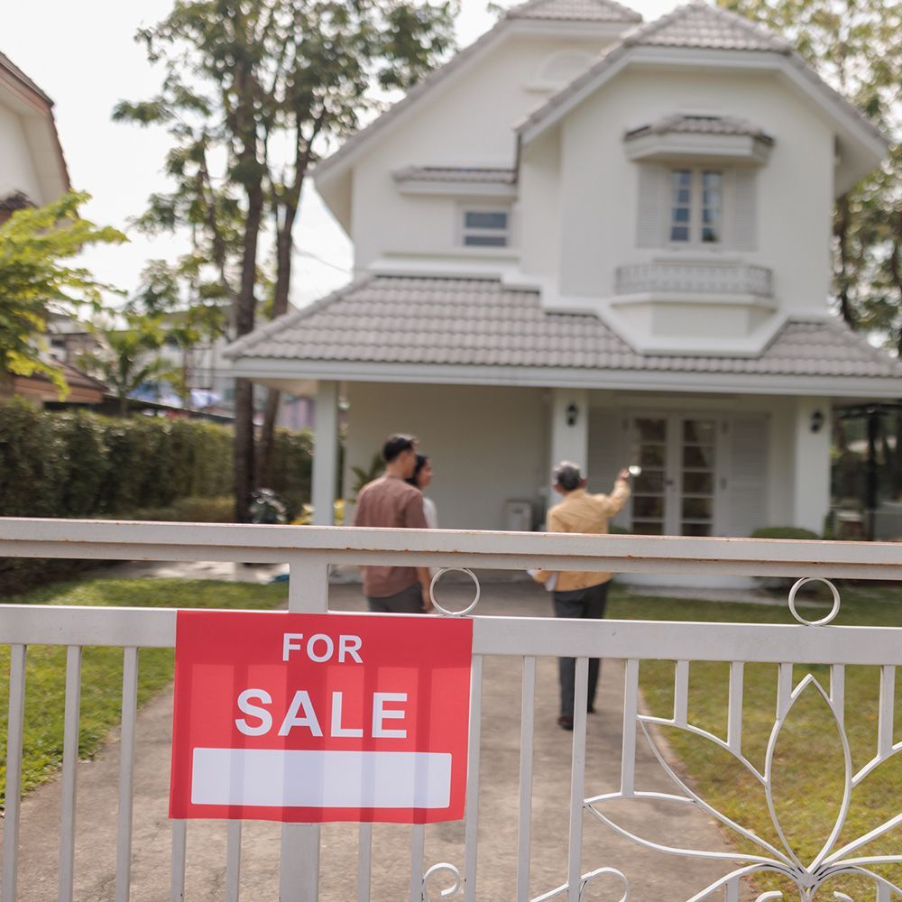 In the yard, potential buyers are looking at the house with a for-sale sign with a real estate agent.
