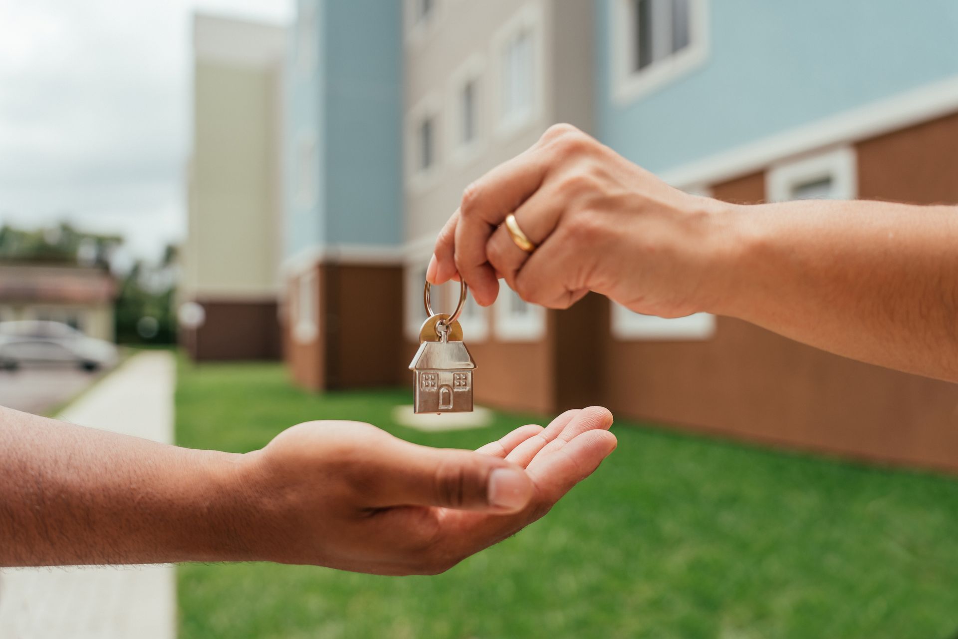 Close-up of a person's hands handing over home keys to a different person, with a building behind.