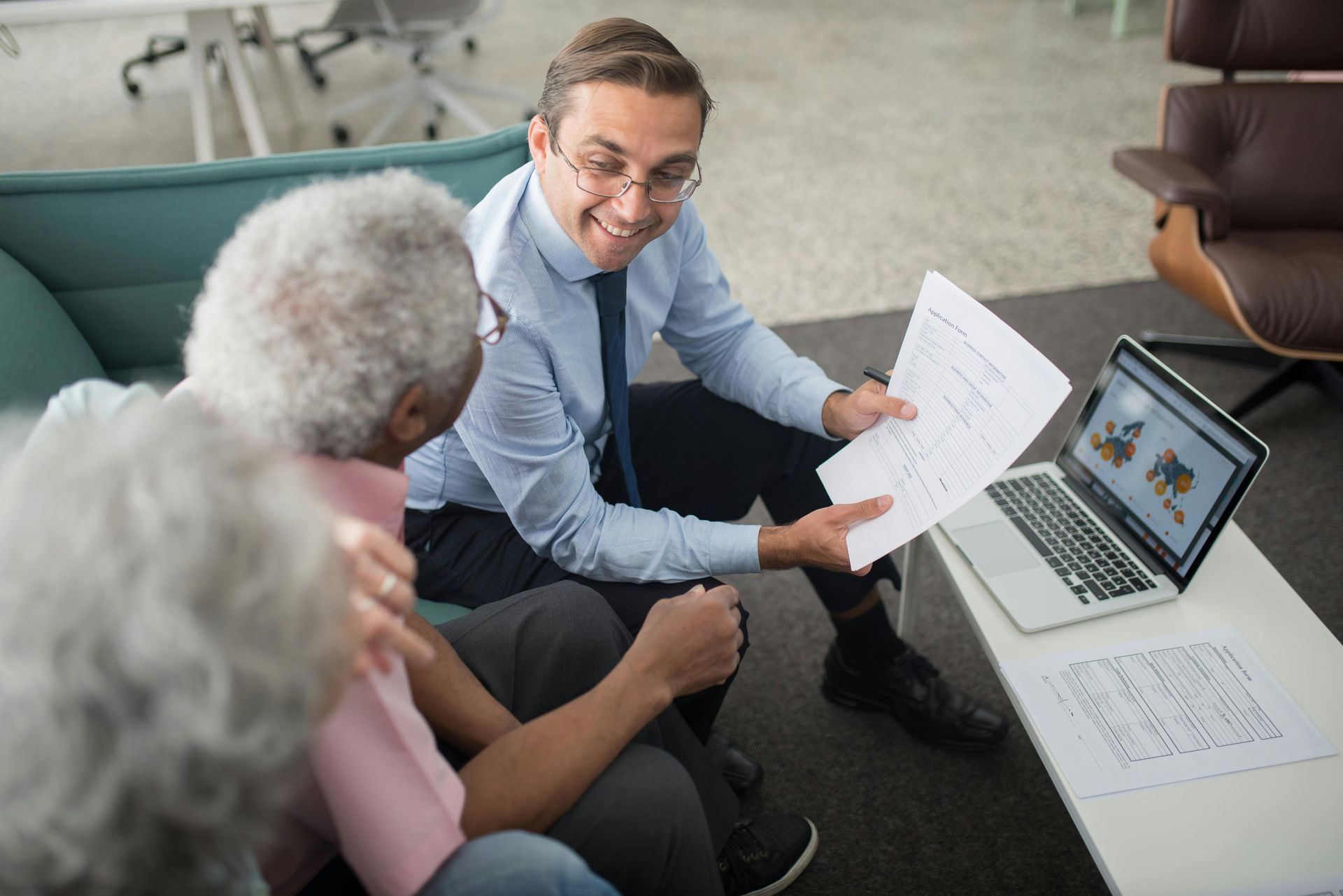 Financial advisor showing documents and laptop to a couple on a sofa.